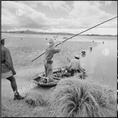 Des soldats français sur une barque en bambou surveillant la récolte du riz.