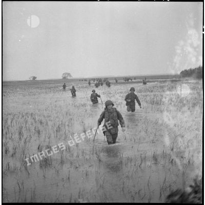 Progression de soldats casqués et armés dans les rizières de Thu Loi.
