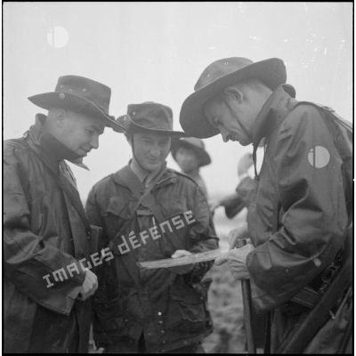Trois soldats, revêtus de leurs pardessus, lisent une carte.