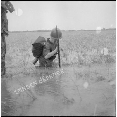 Fusil à la main, un soldat progresse dans l'eau des rizières.