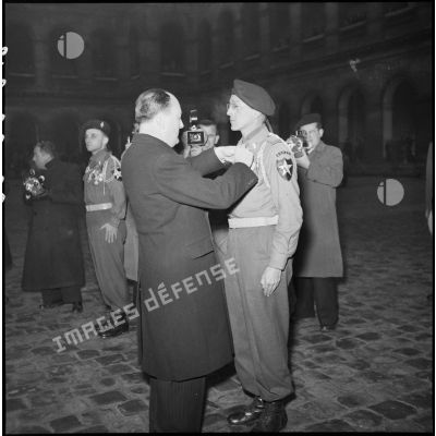 Lors d'une prise d'armes dans la cour d'honneur de l'Hôtel national des Invalides, Pierre de Chevigné, secrétaire d'Etat à la Guerre, remet la croix de la Légion d'honneur au lieutenant Lalager, appartenant au 1er Bataillon Français des Nations Unies (Bataillon de Corée).