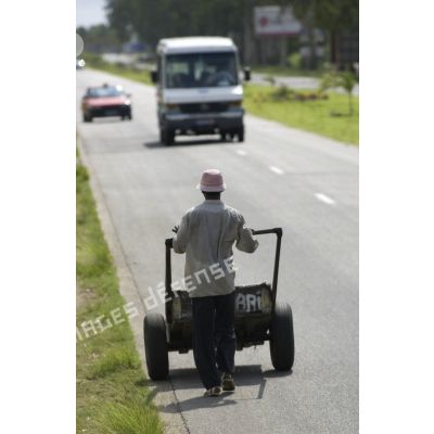 Vie quotidienne à Abidjan. Un homme pousse un chariot artisanal sur le bord d'une route.