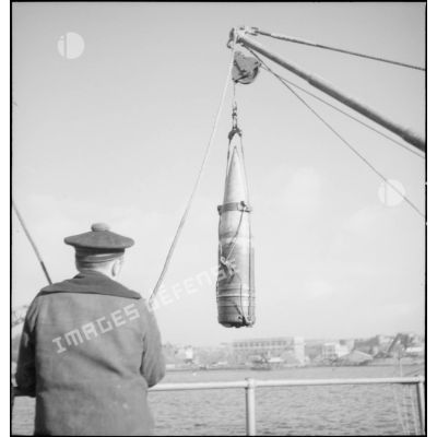 Un marin manipule un obus de 330 mm suspendu à un palan à bord du cuirassé Dunkerque.