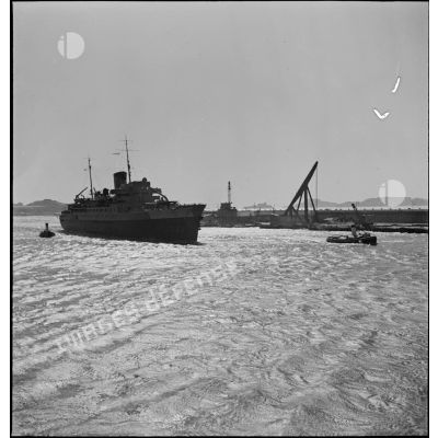 Le paquebot transport de troupes Ville d'Alger est pris en charge par des remorqueurs dans le port de Marseille.