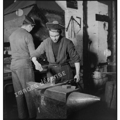 Atelier central de la flotte : un marin forge une pièce de métal.