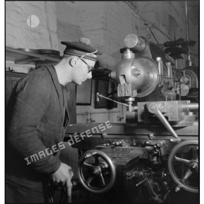 Atelier central de la flotte : un marin travaille une pièce de métal à la fraiseuse.