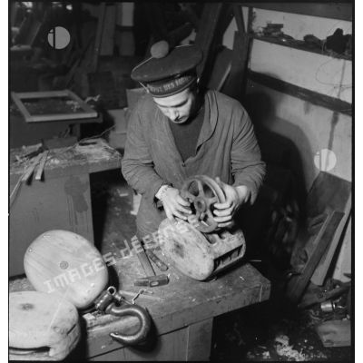Atelier central de la flotte : un marin assemble des poulies pour fabriquer des moufles.