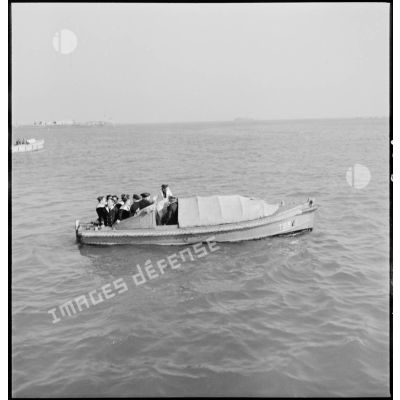 Des marins permissionnaires, vraisemblablement membres d'équipage d'un escorteur (classe T53), se rendent à terre à bord d'une chaloupe.