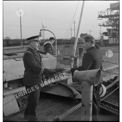 Un capitaine de corvette de la Marine nationale, qui prend possession d'un cargo danois saisi, remet le pavillon du navire à un des officiers du bord.