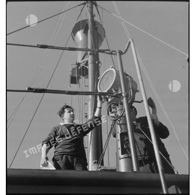 Deux matelots utilisent un projecteur à bord d'un chalutier réquisitionné et armé par la Marine nationale.