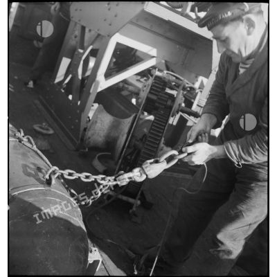 Un marin fixe une chaîne d'amarrage sur un cochonnet de drague à bord d'un chalutier réquisitionné par la Marine nationale comme dragueur de mines.