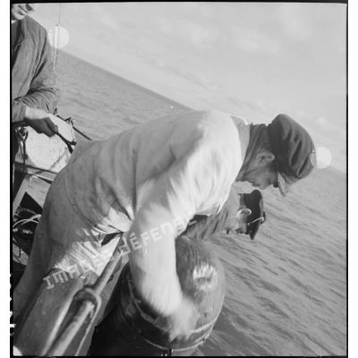 Des marins mettent à l'eau un cochonnet de drague depuis le bord d'un chalutier réquisitionné par la Marine nationale pour servir en qualité de dragueur de mines.