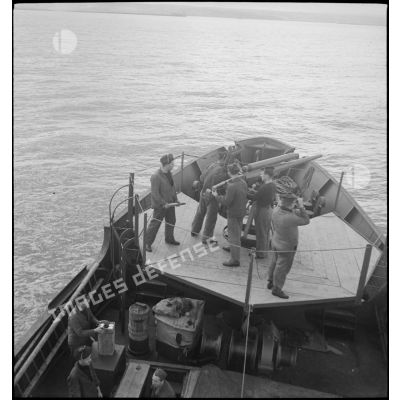 Chargement d'un canon de 75 mm sur la plage avant d'un chalutier réquisitionné et armé par la Marine nationale pour servir de dragueur de mines.