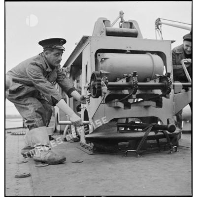 Un second maître manoeuvre le grenadeur de sillage - à chaînes à maillons avec engrenage Galle - de grenades sous-marines, à bord du torpilleur léger Branlebas.