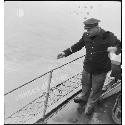 Un second maître pêche à la ligne à bord du torpilleur léger Branlebas.