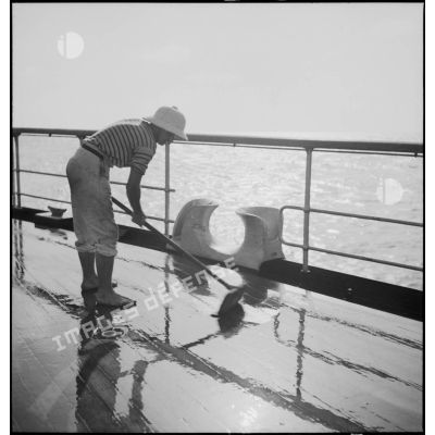 Un marin nettoie le pont du croiseur Strasbourg  naviguant au large de l'Afrique occidentale française (AOF).