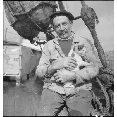 Portrait d'un marin pêcheur et d'un chat mascotte, à bord du chalutier de la marine marchande Roche noire, réquisitionné et armé par la Marine nationale.