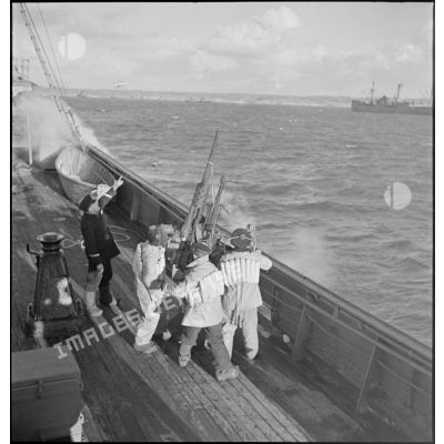 Des canonniers pointent un canon antiaérien de 37 mm à bord d'un cargo naviguant en convoi, réquisitionné et armé par la Marine nationale.