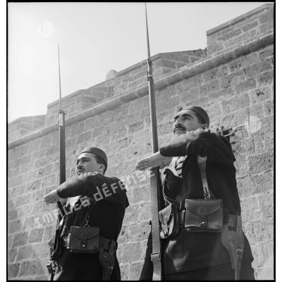 Deux sentinelles d'une unité de défense côtière, canonniers marins algériens, dits Baharia, sont en faction au fort de Mers-el-Kébir et  présentent les armes.