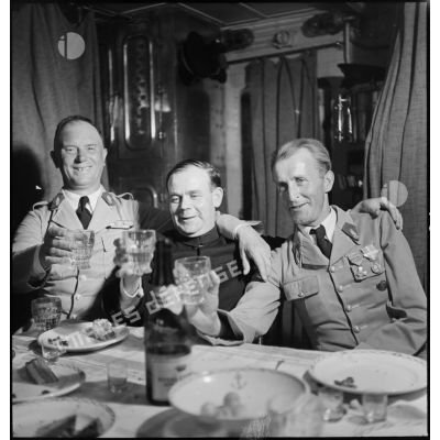Des sous-officiers du 1er régiment étranger d'infanterie (REI) trinquent avec un aumônier lors d'un repas à bord du contre-torpilleur L'Indomptable.
