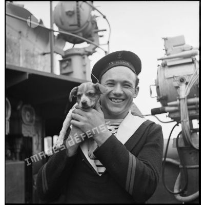 Portrait d'un quartier-maître du contre-torpilleur Le Malin avec un petit chien mascotte.