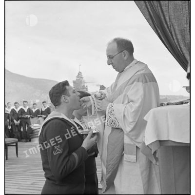 L'aumônier du cuirassé Dunkerque donne la communion à un quartier-maître lors d'une messe célébrée à bord du navire.