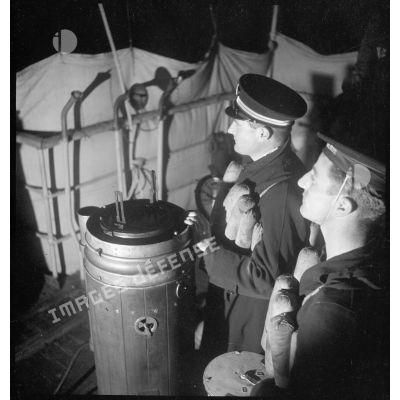 Un enseigne de vaisseau et un matelot sont de veille sur la passerelle lors d'une mission de dragage de nuit, à bord d'un chalutier de la marine marchande, réquisitionné par la Marine nationale.
