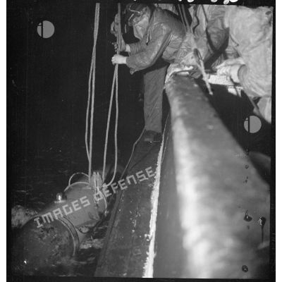 Au cours d'une mission de dragage de nuit, des marins mettent à l'eau le cochonnet de drague depuis un chalutier réquisitionné par la Marine nationale.