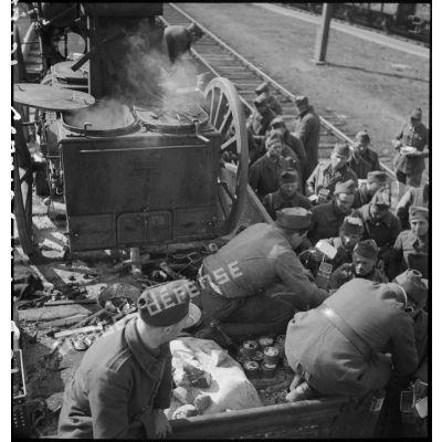 Des soldats perçoivent leur ration pour le repas le long d'une voie ferrée en gare de Trappes.