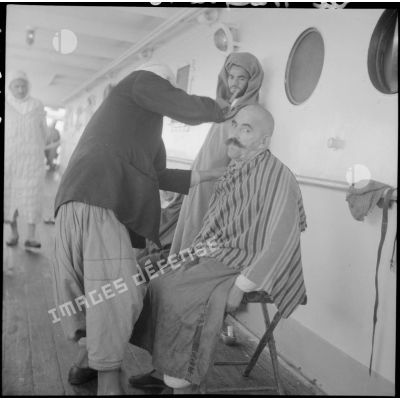 Un pèlerin se fait raser la tête dans une coursive du paquebot "Gouverneur général Gueydon" qui transporte les pèlerins à la Mecque.
