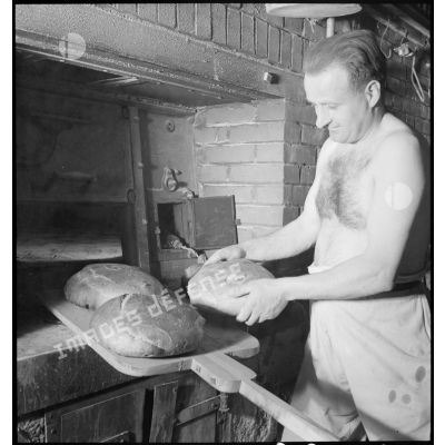 Des boulangers militaires sortent des pains du four et les rangent sur des étagères.