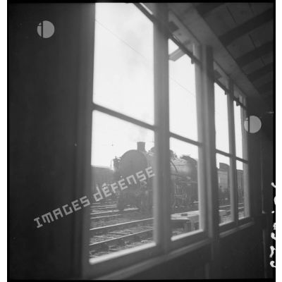 En gare de Trappes une locomotive est photographiée au travers de la fenêtre d'un baraquement.