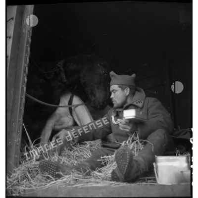 Un soldat mange assis à la porte d'un wagon de marchandises.