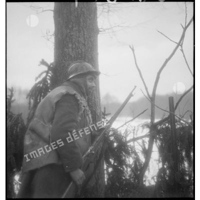Un soldat se tient posté derrière un arbre.