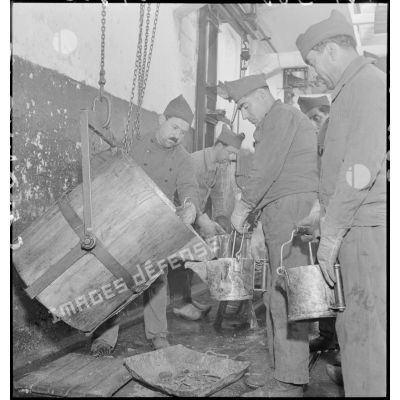 Un ouvrier verse de la mélinite dans de petits récipients tenus par d'autres ouvriers.