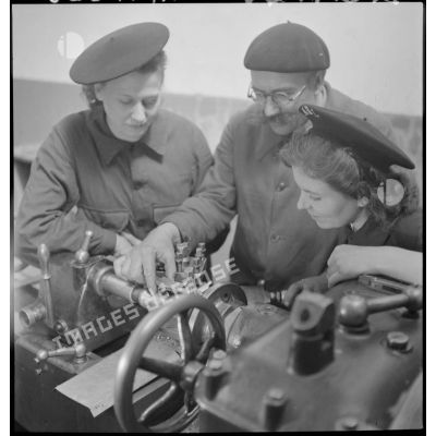 Un professeur assiste deux élèves féminines qui travaillent sur une machine-outil en atelier.