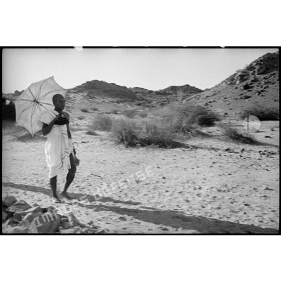 Un pèlerin en tenue d'irham marche dans le désert en tenant une ombrelle.