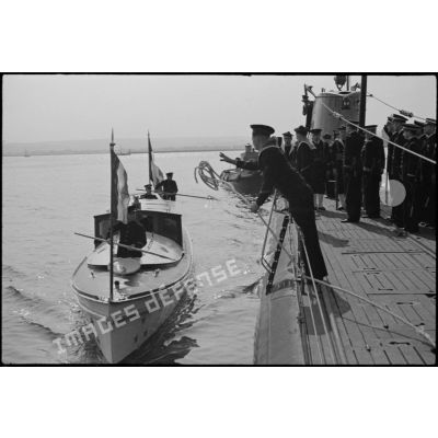 La vedette transportant le vice-amiral Jules Le Bigot, préfet maritime de Cherbourg, arrive le long du bord du sous-marin Orphée.