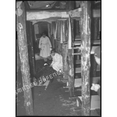 A l'intérieur d'un poste de secours de campagne deux infirmiers militaires s'occupent d'un blessé couché sur un brancard.