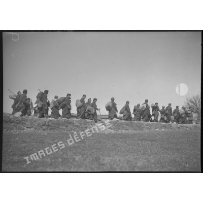 Des soldats marchent sur une route, ils sont photographiés de profil en plan général.
