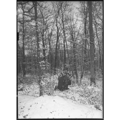 Sous un bois, plan général d'un soldat accroupi dans la neige.