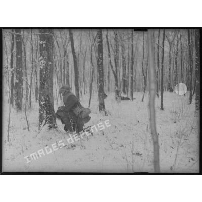 Sous un bois, plan général d'un soldat accroupi dans la neige.