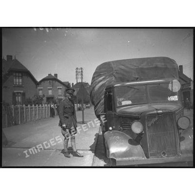 Un officier anglais de la BEF se tient debout près d'un camion de marque Bedford dans un village minier du département du Nord.