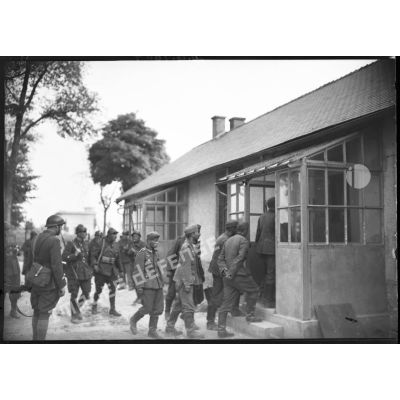 Un groupe de prisonniers allemands rentre dans une maison sous la surveillance de gardes républicains mobiles (GRM) et de soldats français.