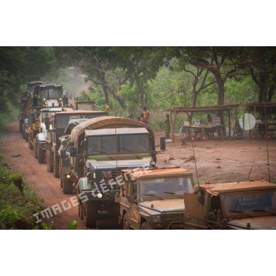 Une colonne de camions formant un convoi logistique dépasse un marché local situé aux abords de la POD (plateforme opérationnelle défense) de Bambari, lors d'un ravitaillement au profit des éléments du GTIA (groupement tactique interarmes) Turco.