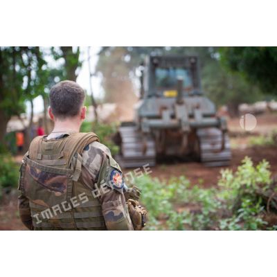 Sous les yeux d'un soldat, un bulldozer Liebherr de type PR 724 LGP du 25e RGA déboise une zone en prévision de la réalisation d'un terrain de football au profit des habitants du village de Makangé.