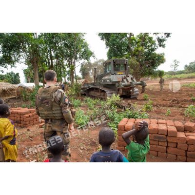 Sous les yeux d'un soldat et d'enfants des environs, un bulldozer Liebherr de type PR 724 LGP du 25e RGA déboise une zone en prévision de la réalisation d'un terrain de football au profit des habitants du village de Makangé.