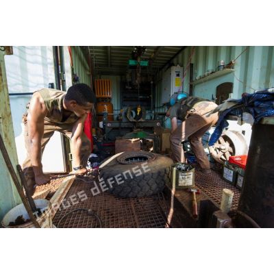Des mécaniciens effectuent une réparation sur la roue d'un véhicule, à l'atelier de réparation mécanique du train de combat du camp de M'Poko de Bangui.