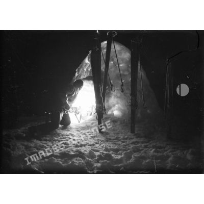 De nuit, un éclaireur-skieur libanais de la 3e DBL se tient à genoux à l'entrée d'un igloo éclairé de l'intérieur.