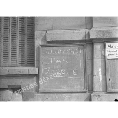 Plan rapproché d'un panneau à l'entrée du lycée Charlemagne indiquant l'arrêt des cours suite au bombardement.